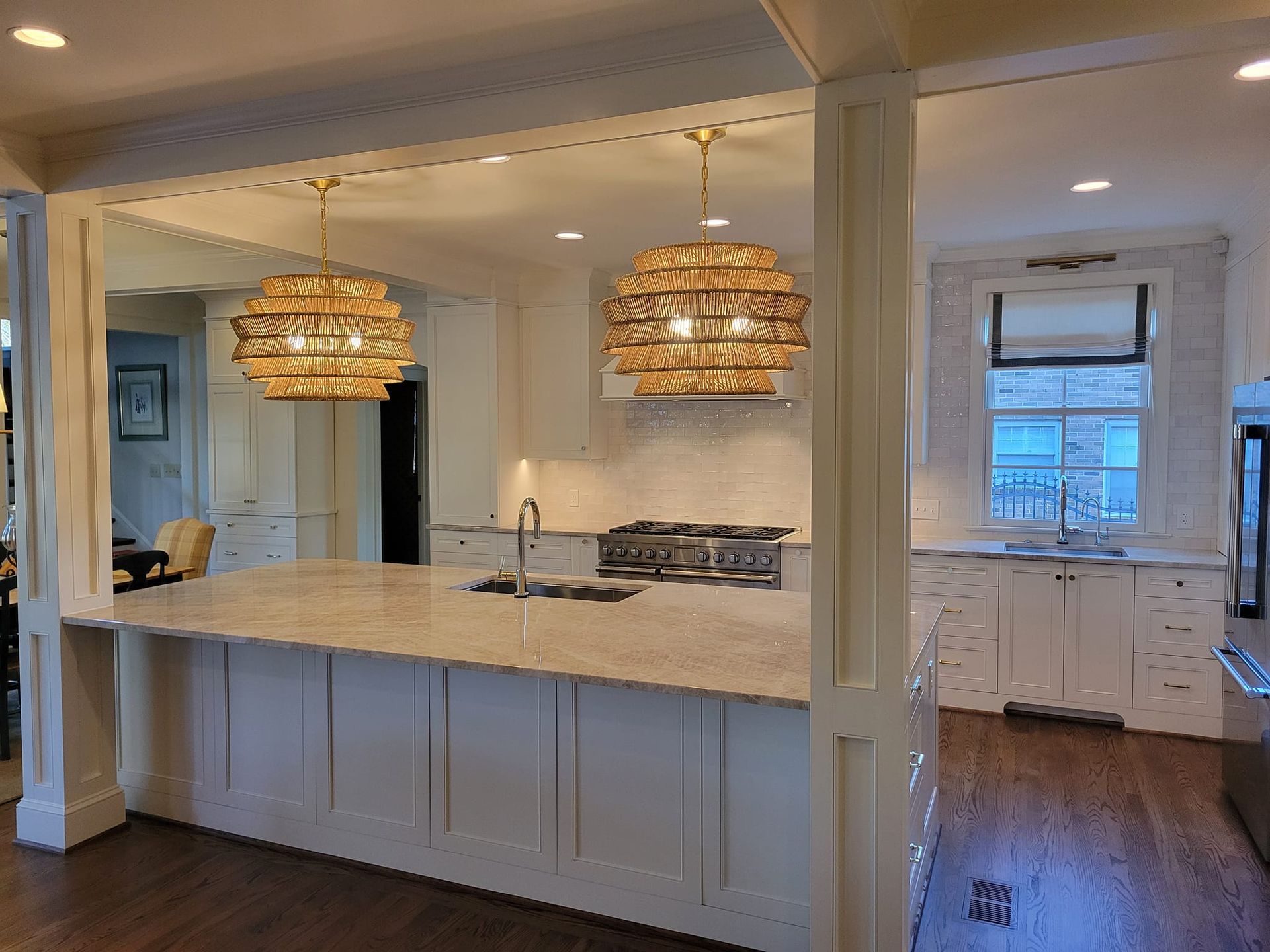 Bright, open kitchen with white cabinets, marble island, wood floors, and two woven pendant lights.