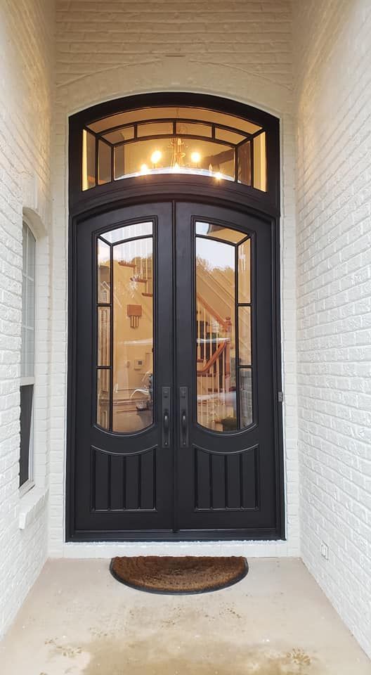 Black double front door with arched transom, flanked by white brick walls and lit entryway.