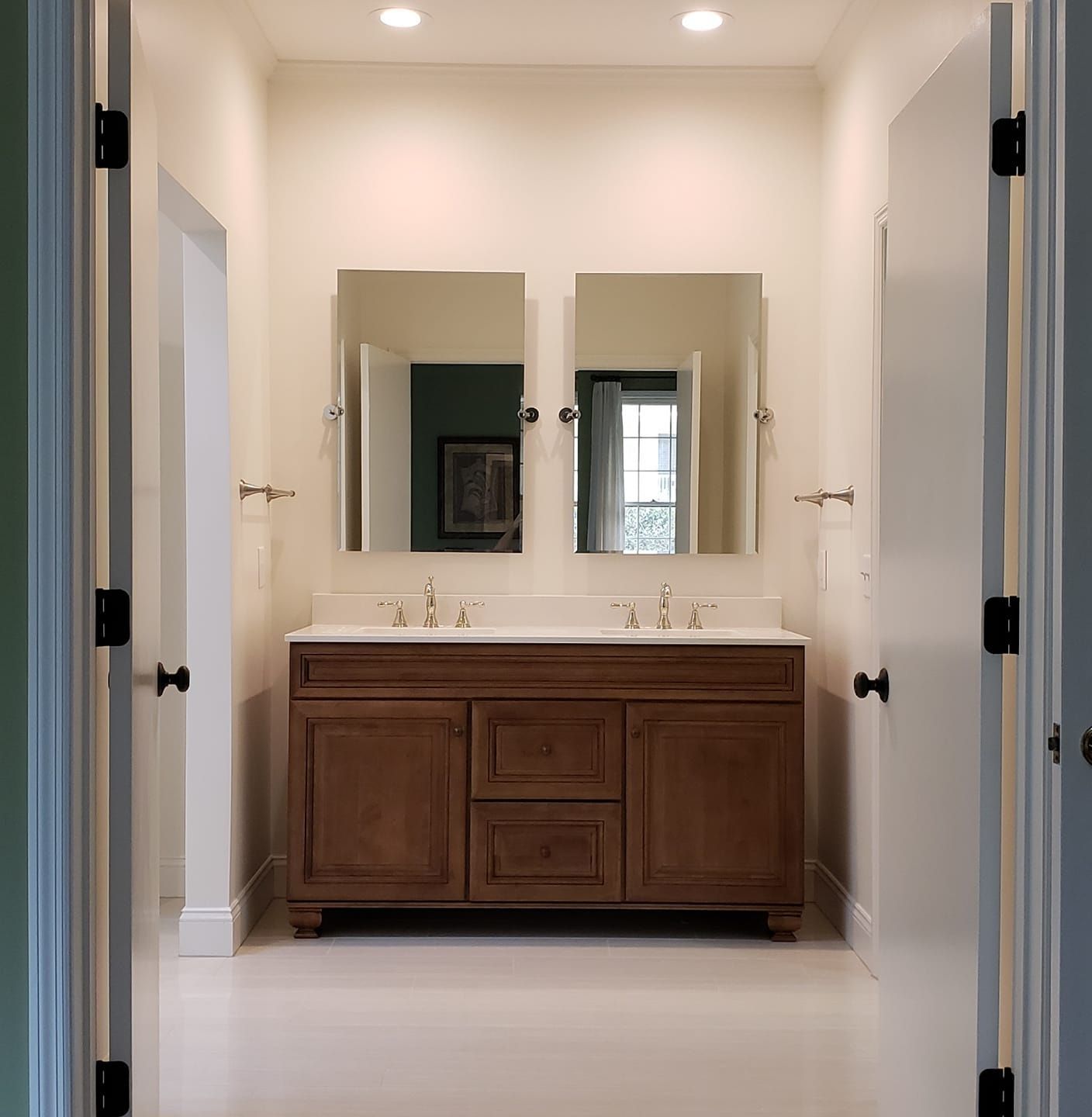 Bright bathroom with a wooden vanity, double mirrors, white walls, and recessed ceiling lights.