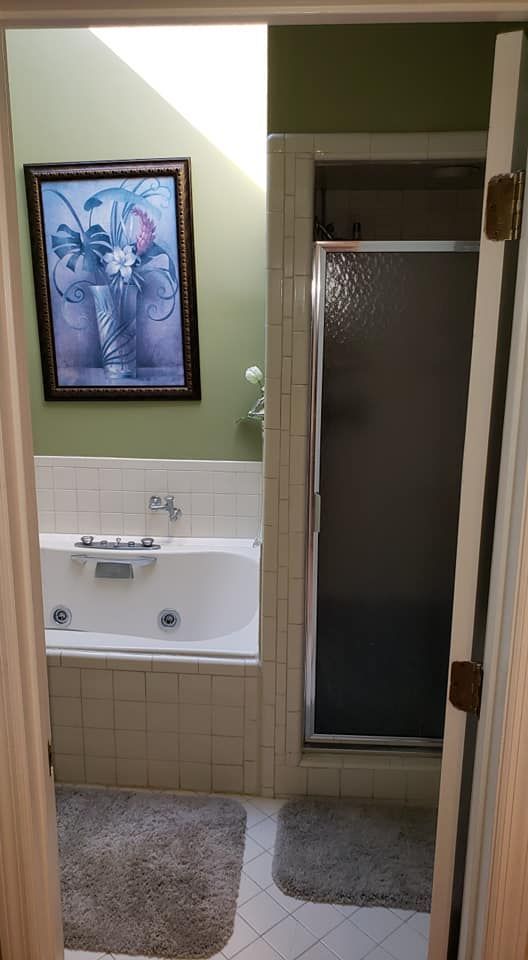Bathroom vanity and sink beside a glass shower, with beige tile, mirror, and framed wall art.