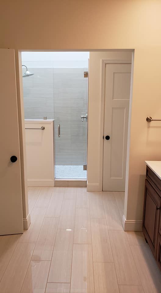 Bright bathroom with open doorway to tiled shower and beige walls, seen from a vanity area