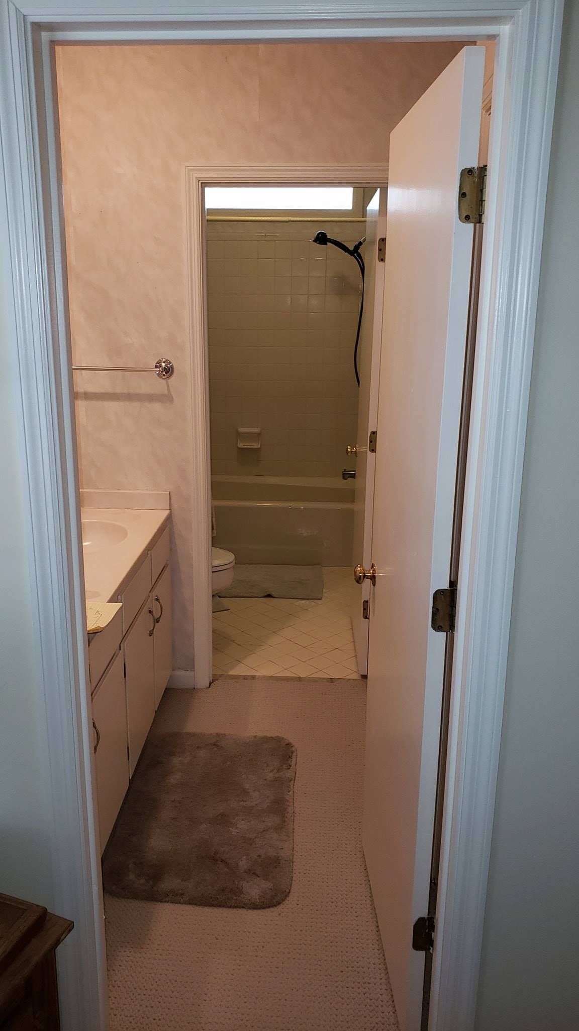 View down a hallway into a bathroom with a bathtub, beige walls, and a white door ajar.