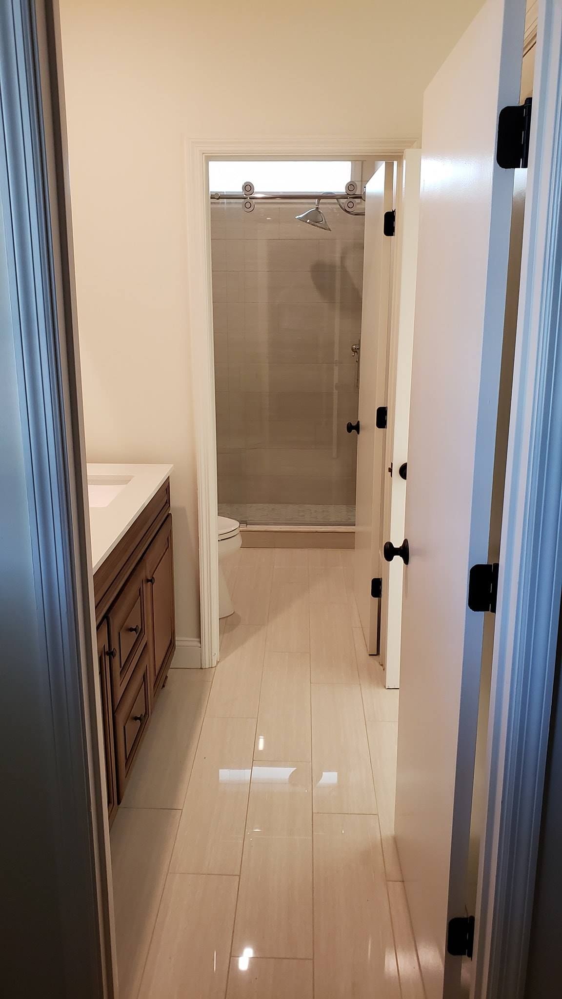Narrow hallway leading to a bathroom with a glass shower door and tiled floor.