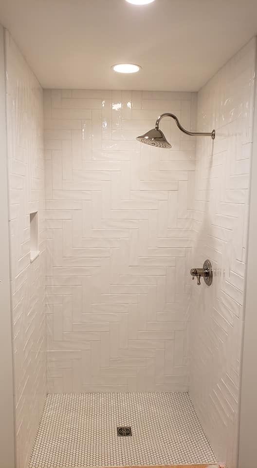 Empty white tiled shower with a chrome showerhead and recessed ceiling light.