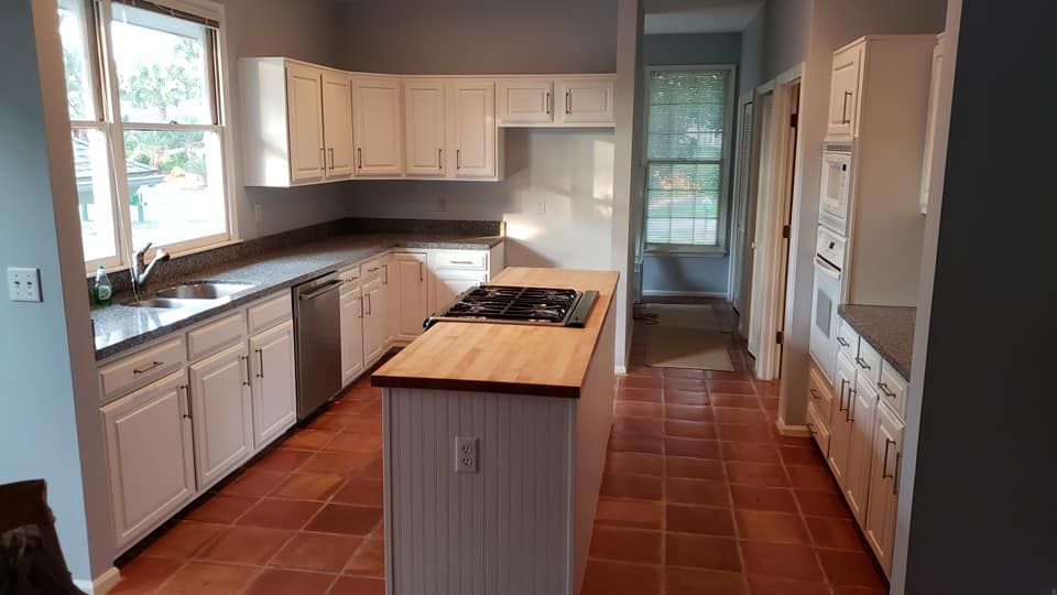 Bright kitchen with white cabinets, terracotta tile floor, and a wooden island counter.