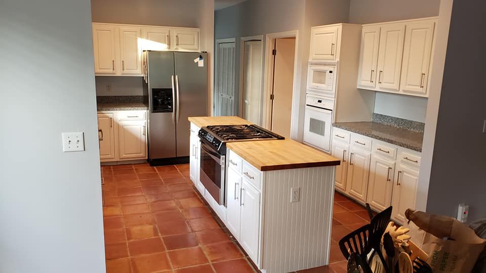 Bright kitchen with white cabinets, stainless fridge, wood island, and terracotta tile floor.