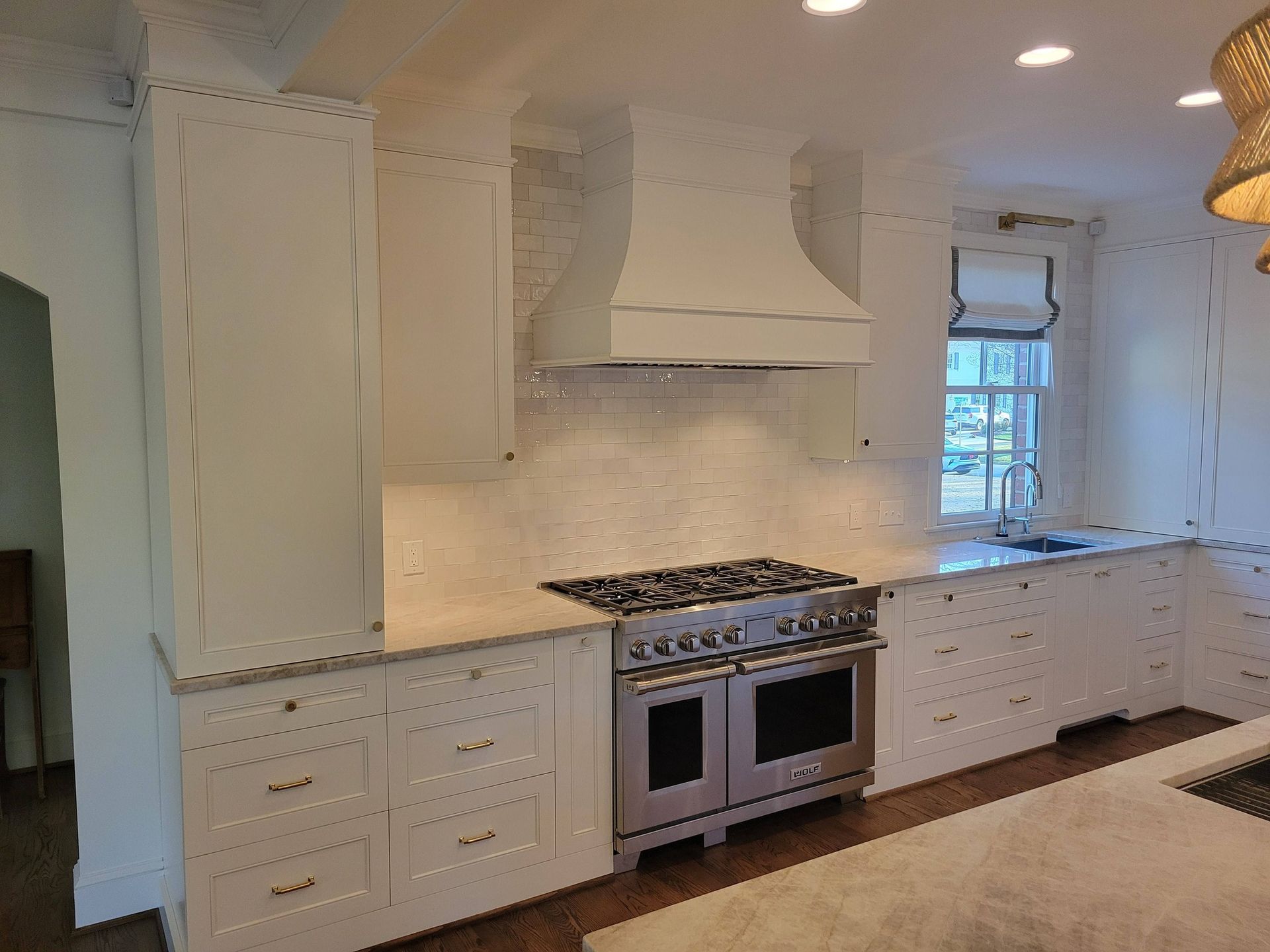 Bright white kitchen with gas range, hood, cabinets, and window