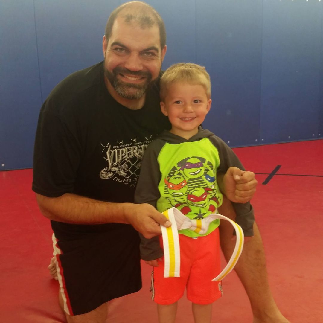 A man is kneeling down next to a young boy in a taekwondo class.