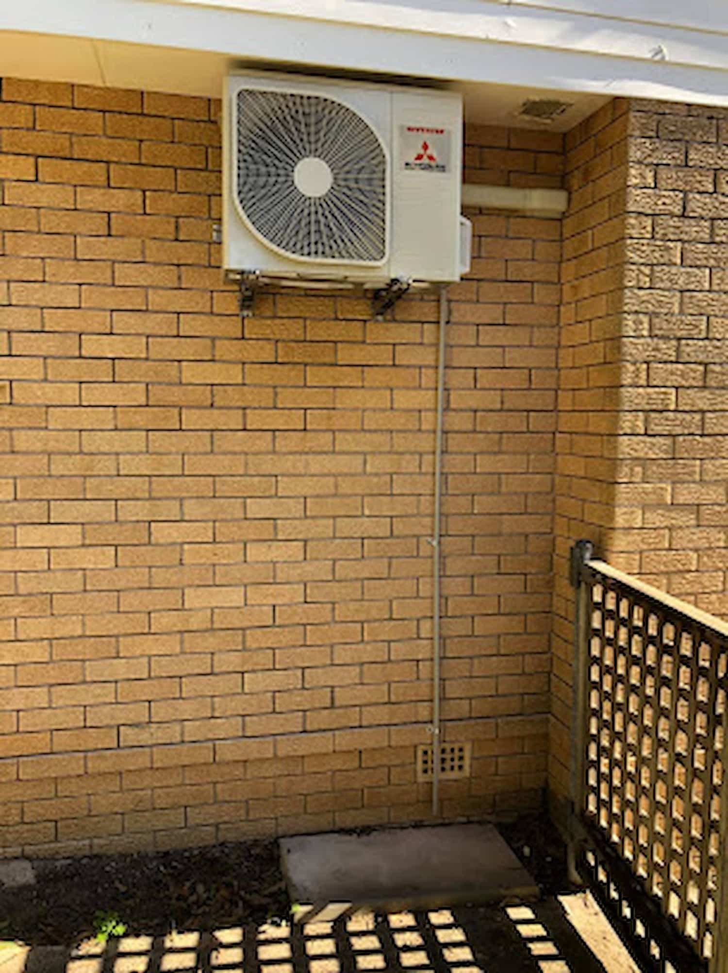Outdoor Brick Wall with A Mounted Air Conditioner and A Small Fenced Area — Steve's Air Conditioning in Kanahooka, NSW