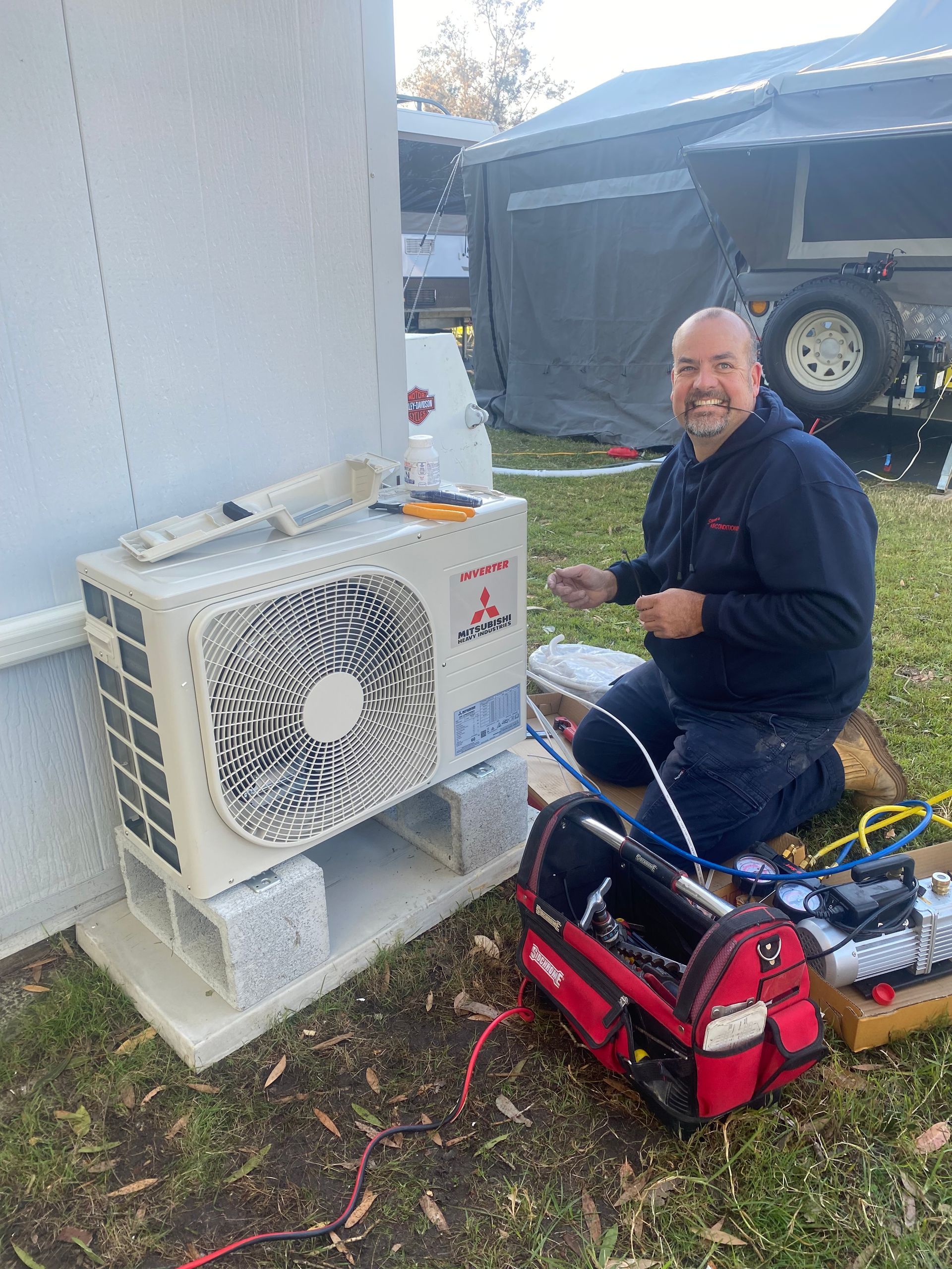 A White Air Conditioner is Mounted on the Side of a Building Next to a Window — Steve's Air Conditioning in Lakeside Dr, NSW