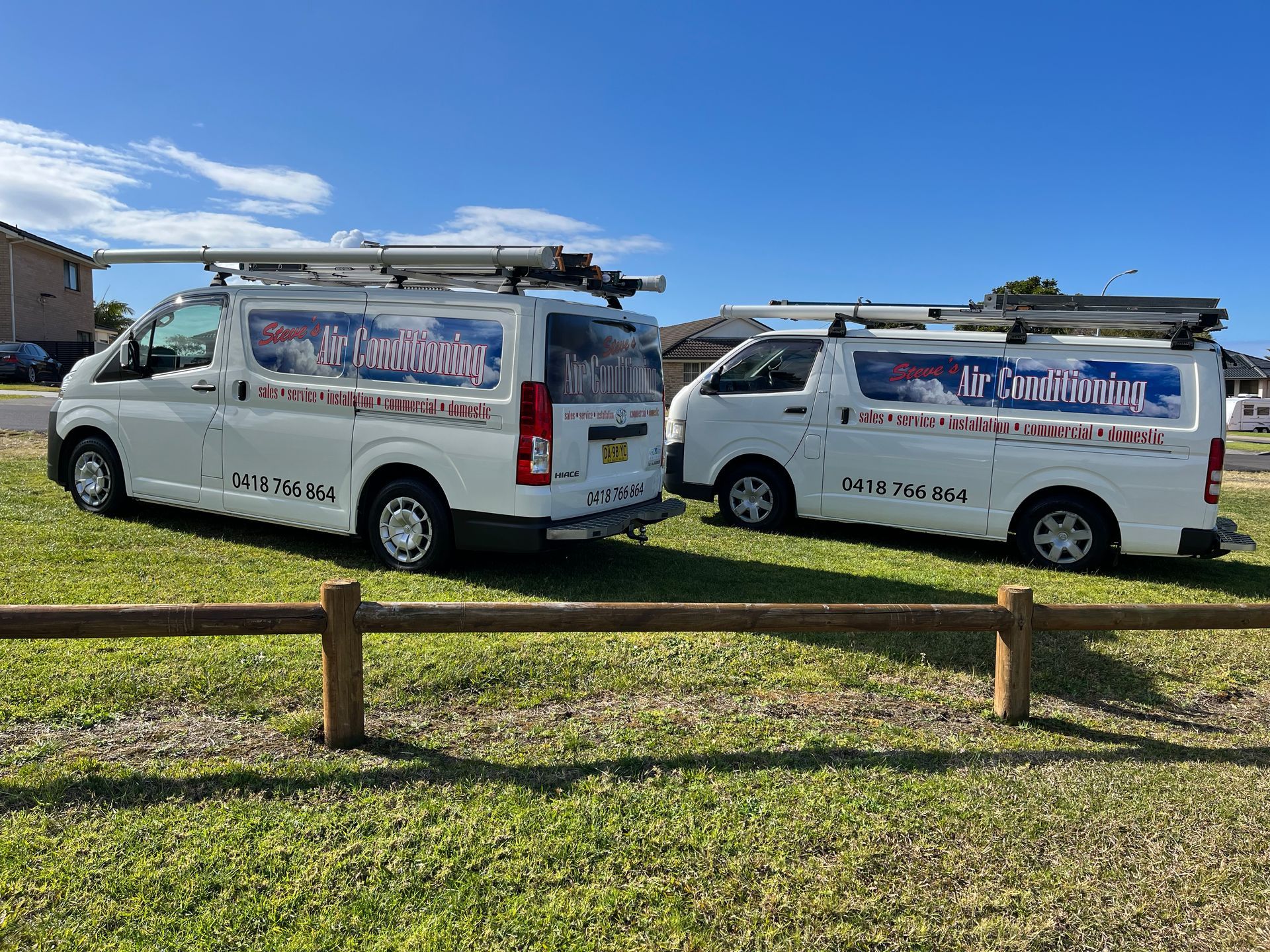 Two white vans are parked next to each other in a grassy field.