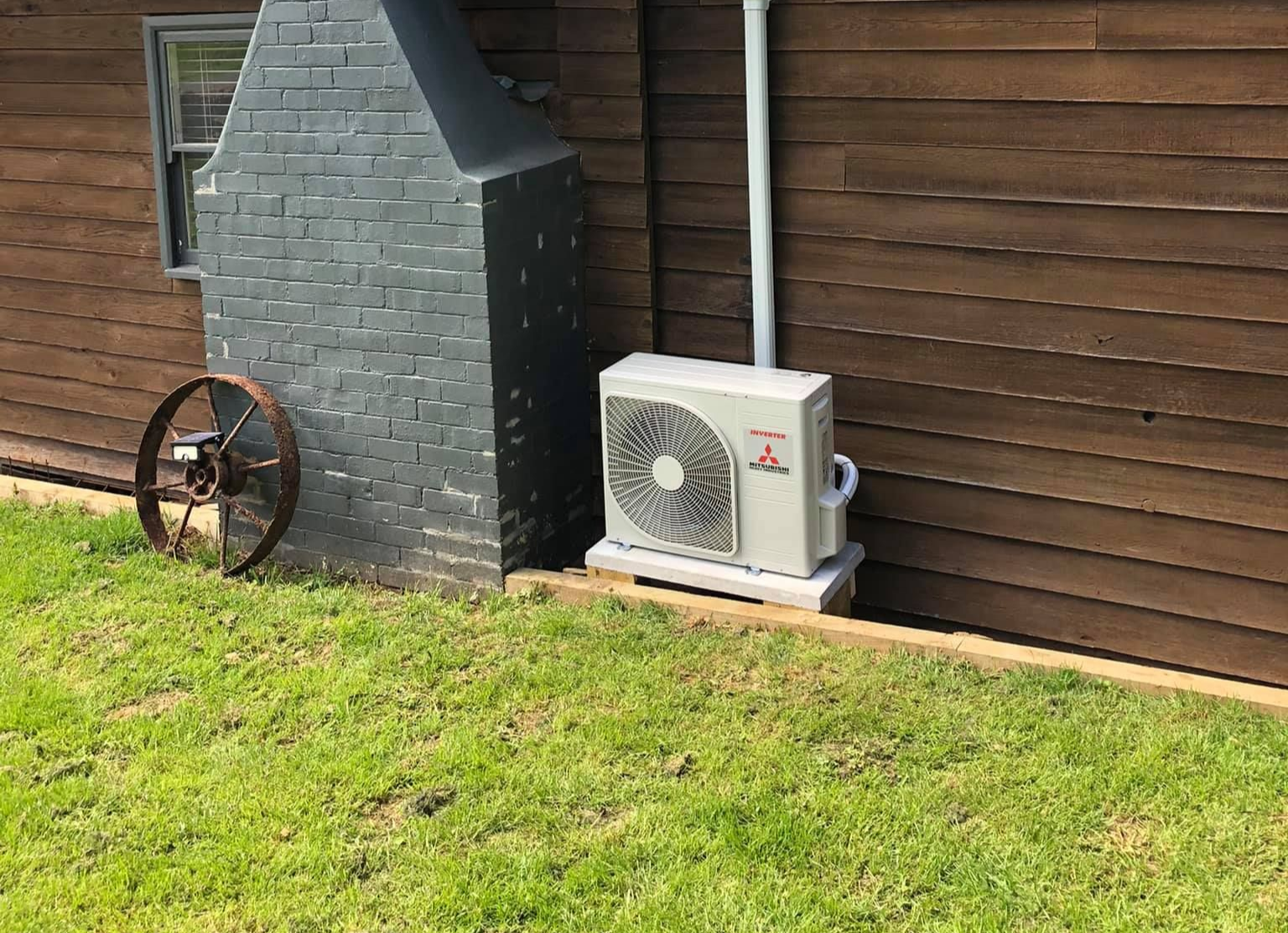 Air Conditioner Unit Beside a Brick Chimney on A Yard Next to A Wooden Wall — Steve's Air Conditioning in Kanahooka, NSW