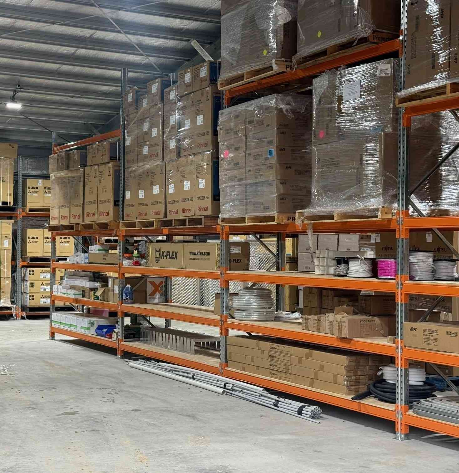Warehouse shelves filled with cardboard boxes and wrapped packages, concrete floor — Magneto HVAC in Tablelands, QLD