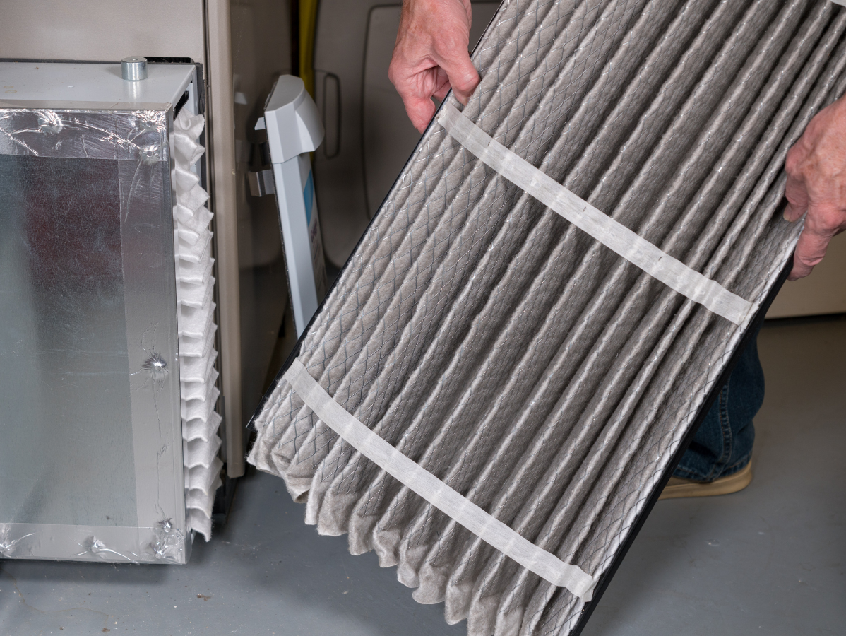 Person holding a dirty air filter, next to a furnace.