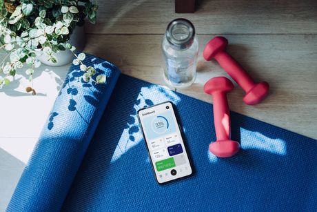 A cell phone is sitting on a yoga mat next to a bottle of water and dumbbells.