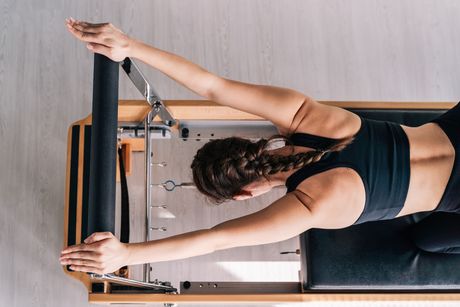 A woman is stretching her arms on a pilates machine.