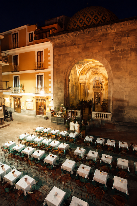 Tavoli da ristorante all'aperto accanto a un arco di pietra storico illuminato di notte