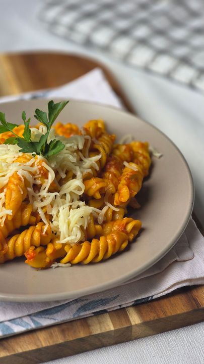 Pasta al sugo di pomodoro e formaggio grattugiato su un piatto, guarnita con prezzemolo su un tagliere di legno.
