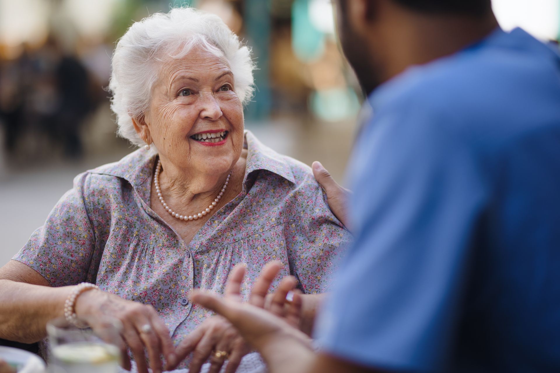 An elderly woman is sitting at a table talking to a nurse.