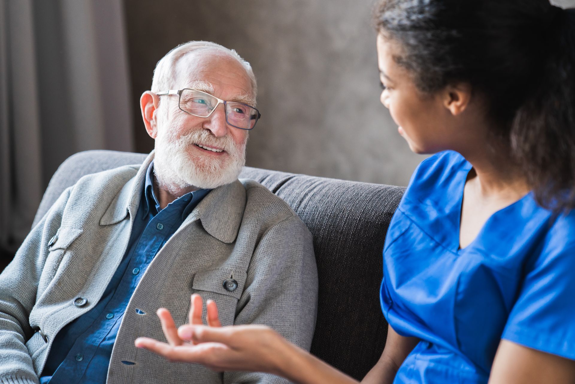 An elderly man is sitting on a couch talking to a nurse.