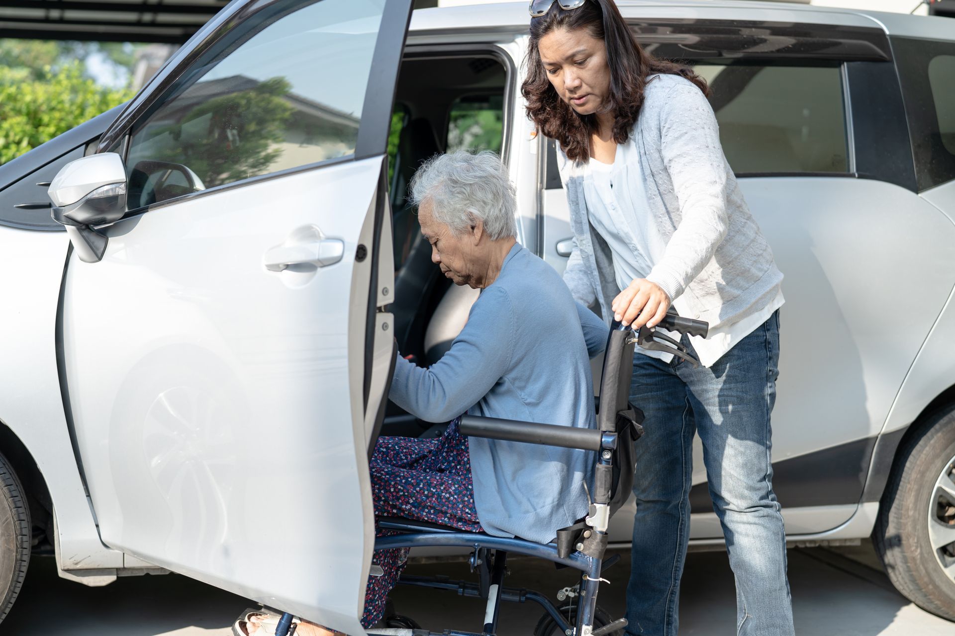 A woman is helping an elderly woman in a wheelchair get out of a car.
