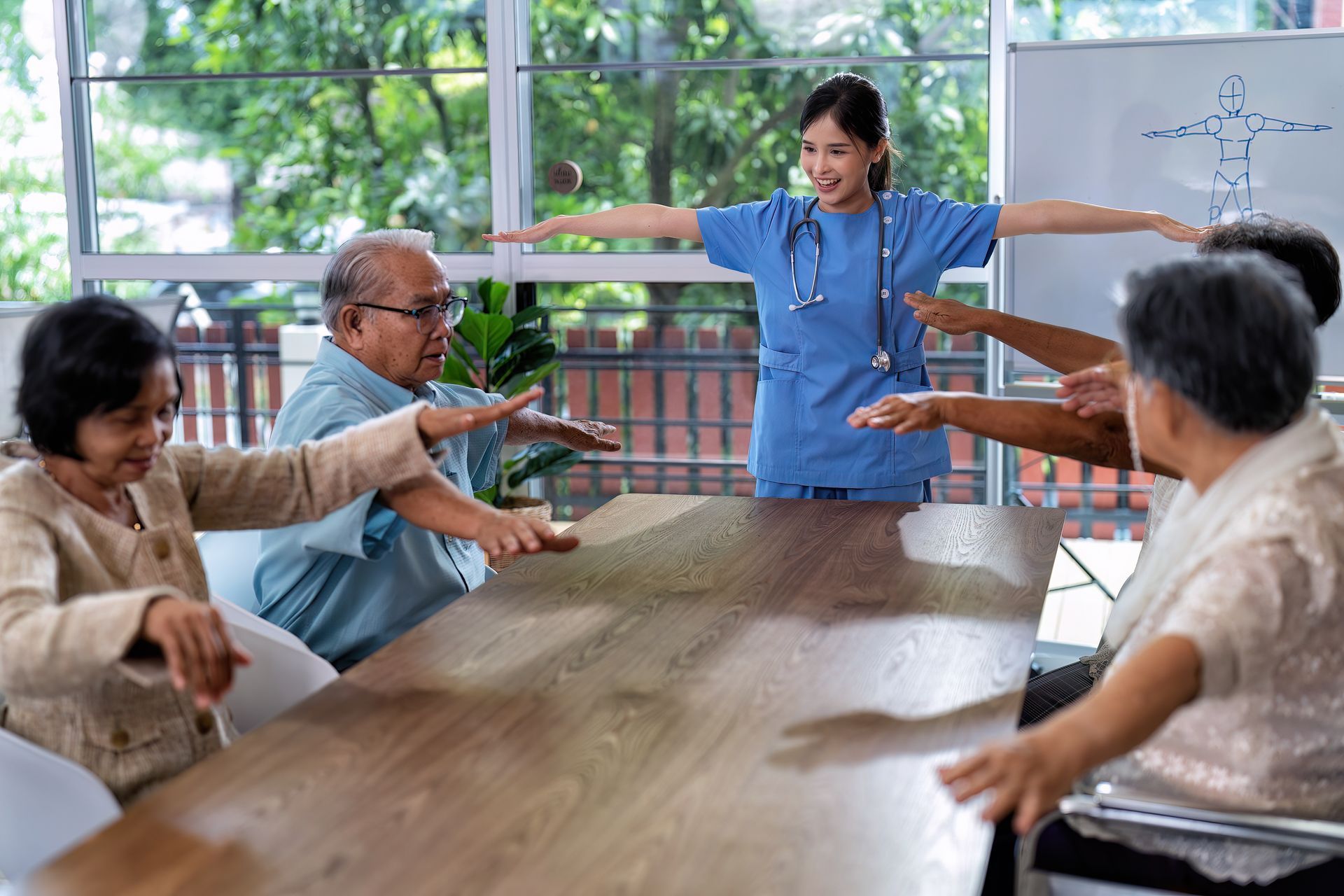 A group of elderly people are sitting around a table with a nurse standing behind them.