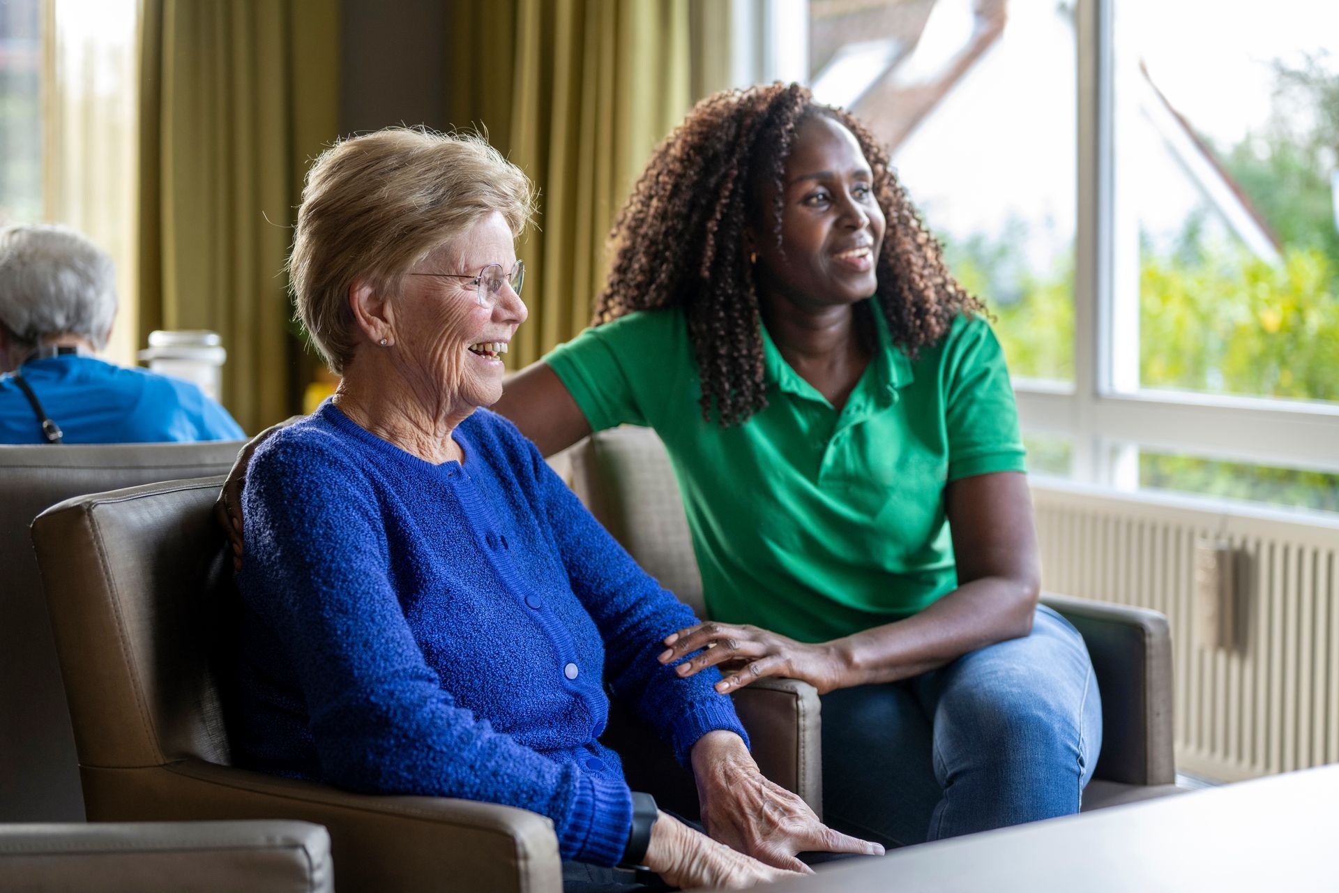 A woman in a green shirt is sitting next to an older woman in a chair.