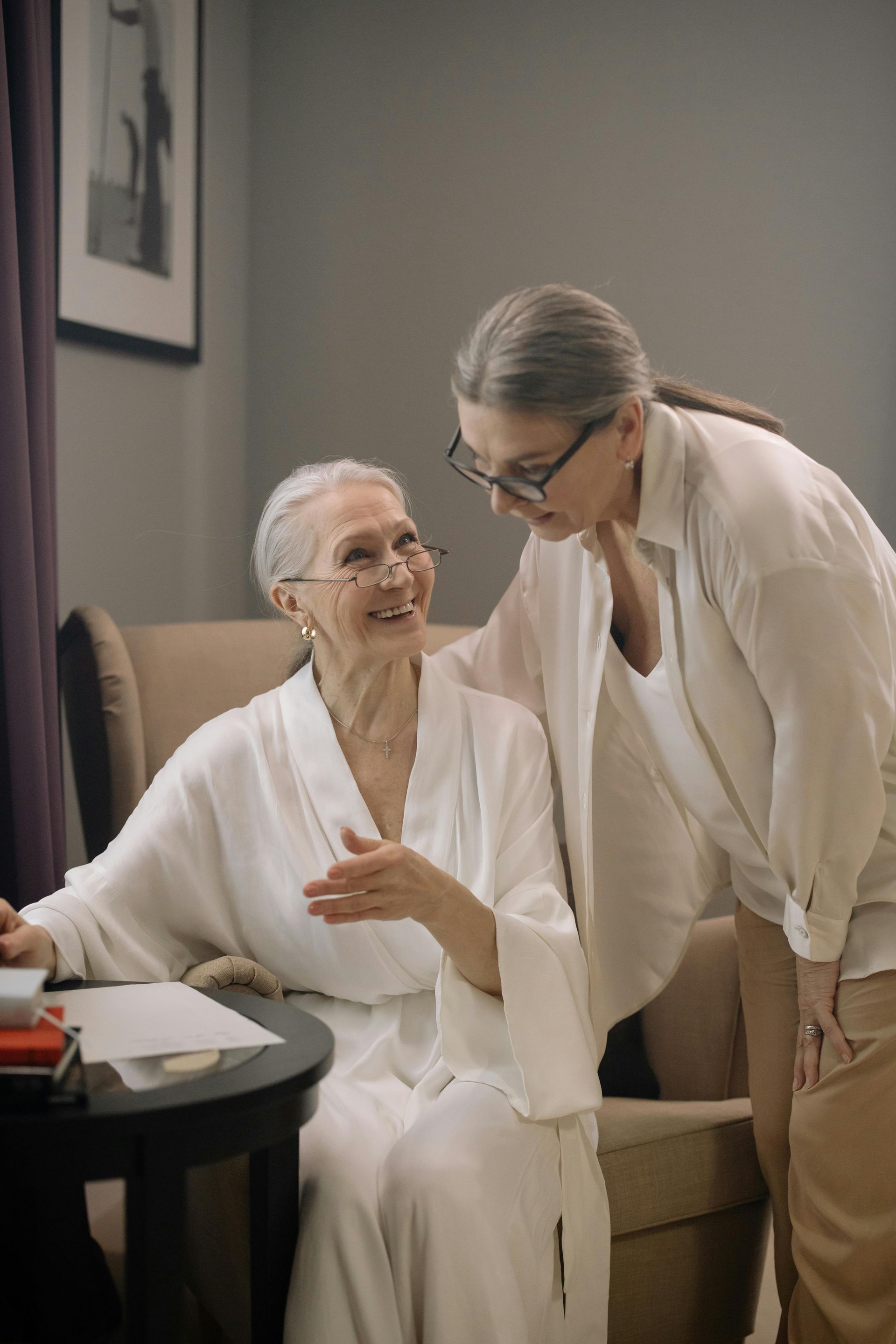 A woman is standing next to an older woman sitting in a chair.