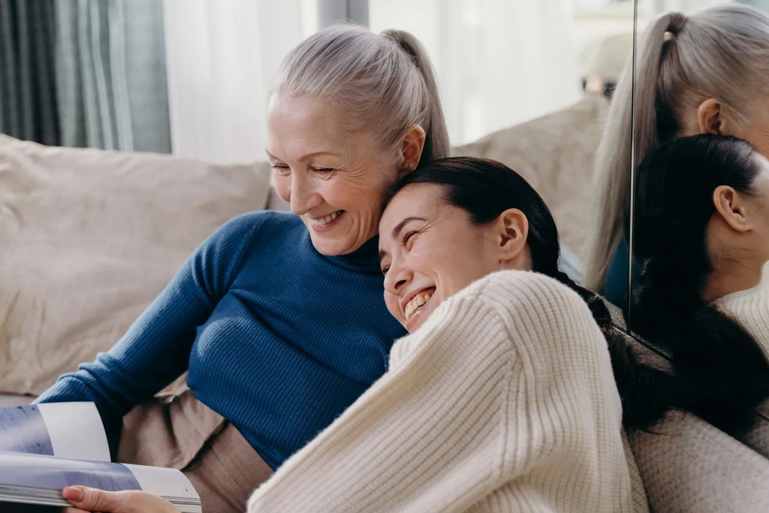 Two women are sitting on a couch looking at a book.