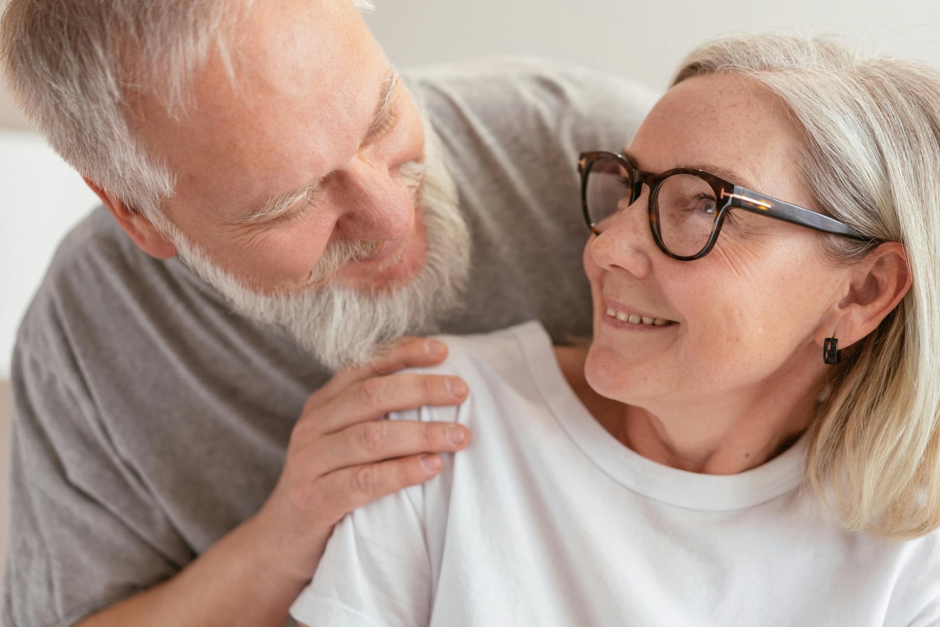 A man and a woman are looking at each other and smiling . the woman is wearing glasses.