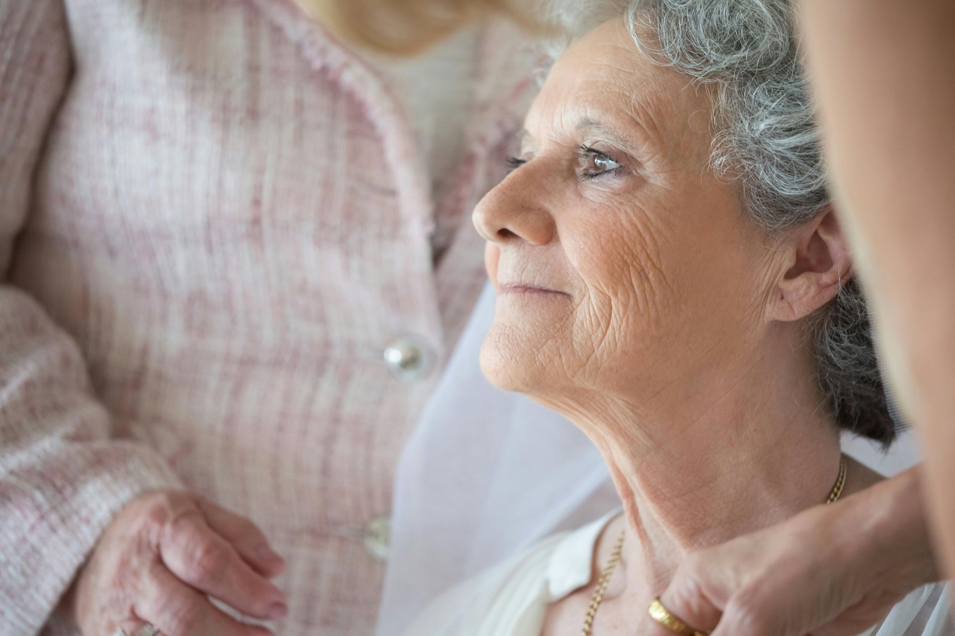 A woman is helping an elderly woman put on a necklace.