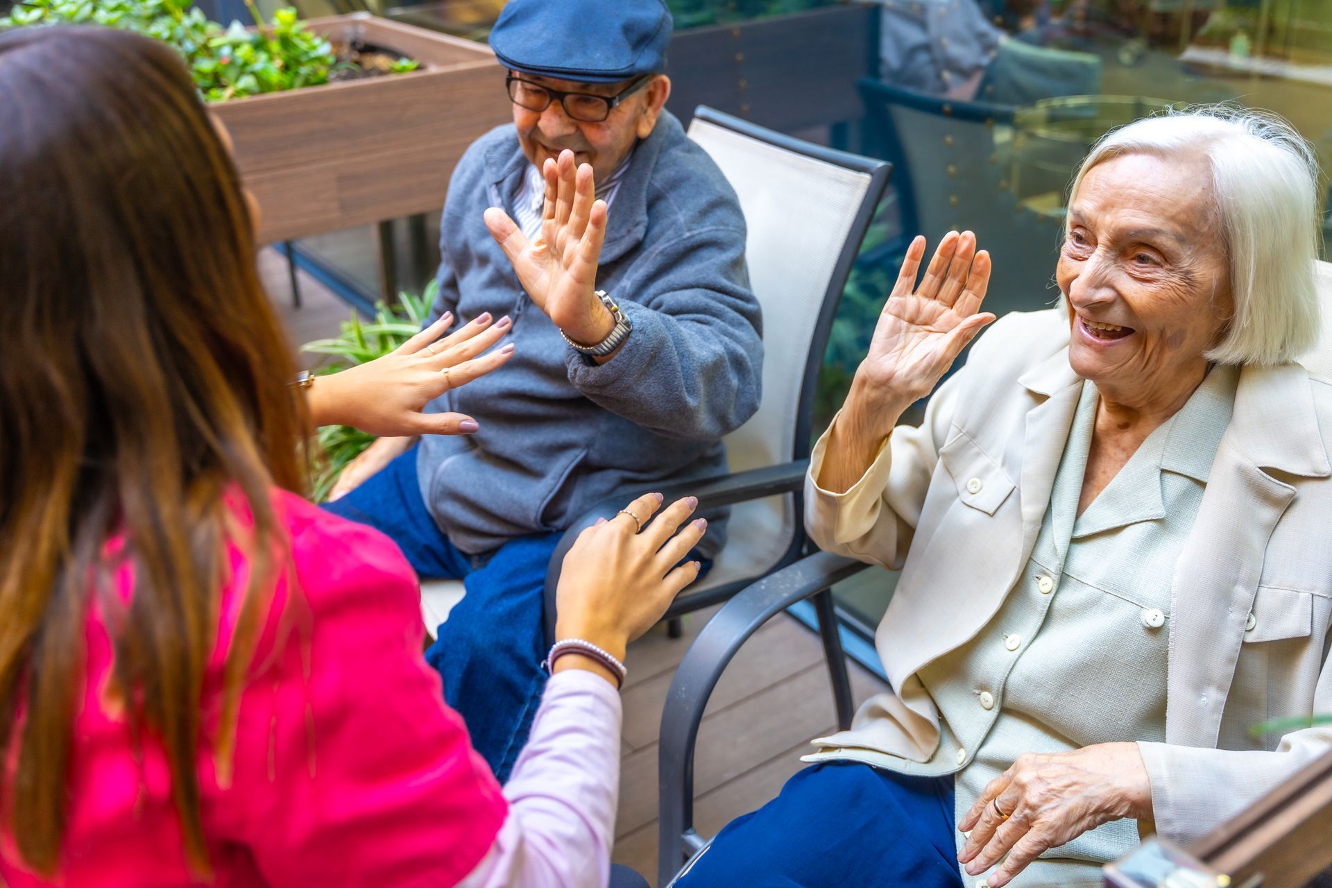 A group of elderly people are sitting in chairs and waving at each other.