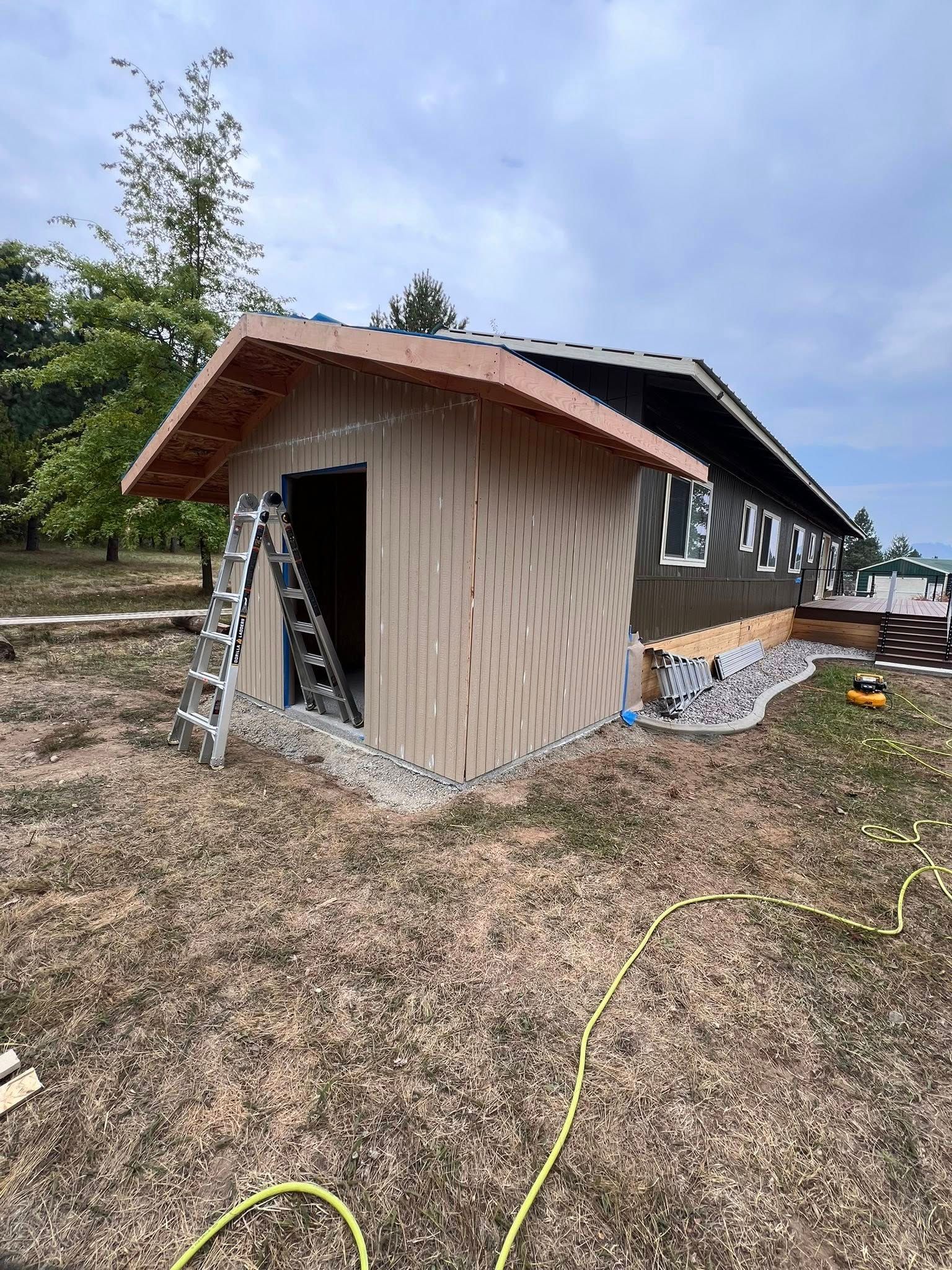 Construction of a light brown building with tan siding, brown roof, and small windows. A ladder and materials are present.