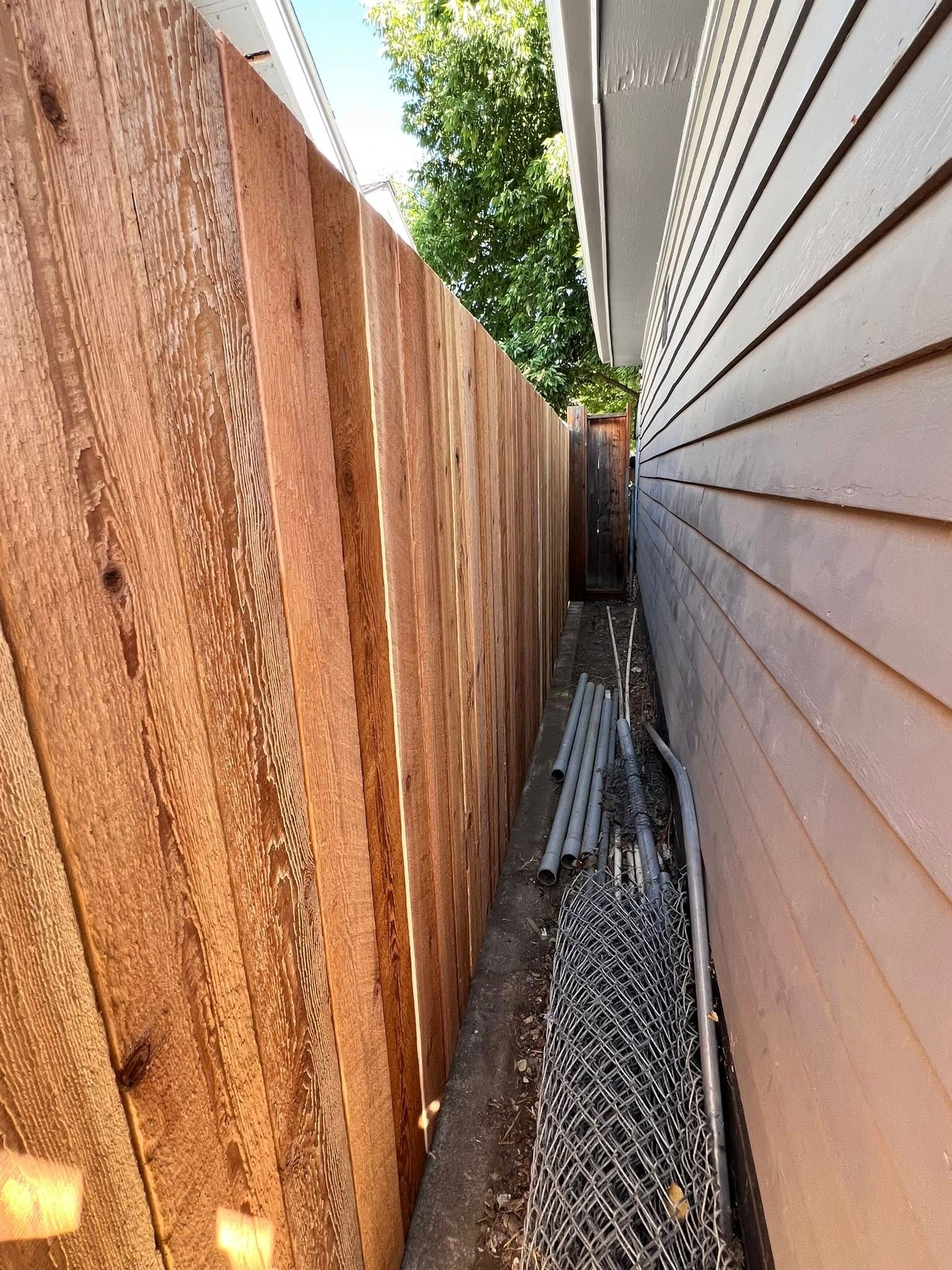 Wooden fence next to a building, narrow space with debris.