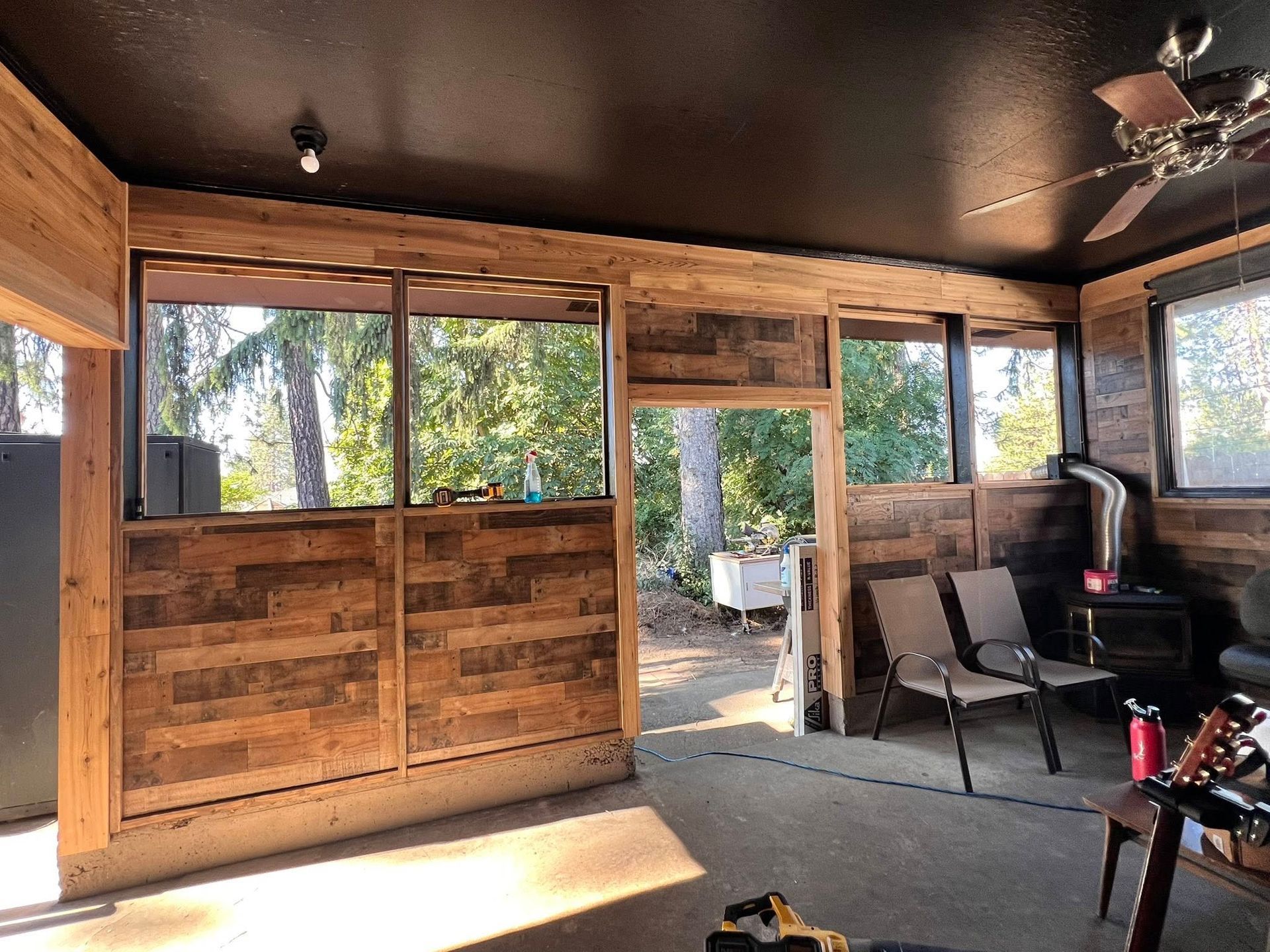 Interior of a room with wood-paneled walls and a black ceiling. Windows offer a view of trees.