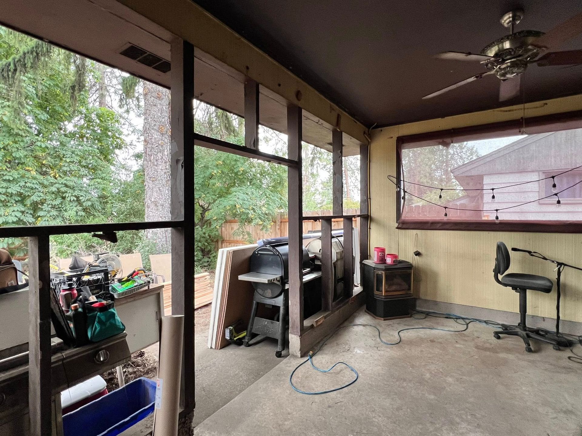 Screened-in porch under construction, with open views of trees. Tools and materials are visible.