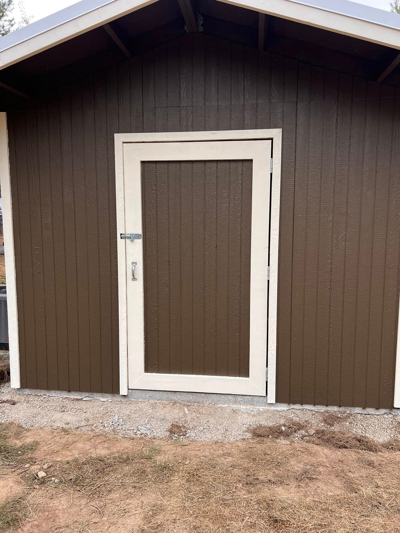 Brown shed with white doorframe and door, gravel base, outdoors.