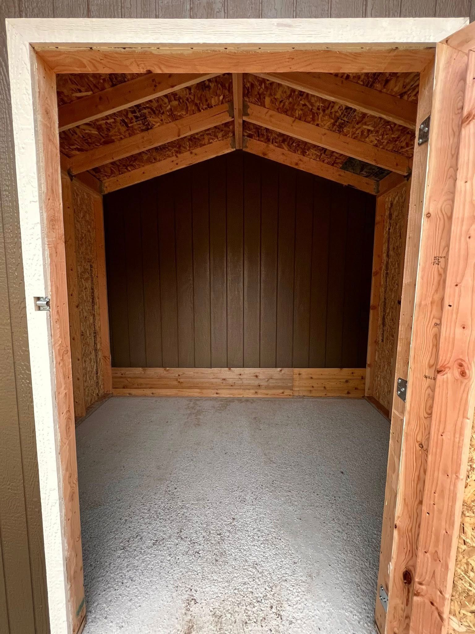 Interior of a small shed, with gravel floor, wooden walls, and open door.