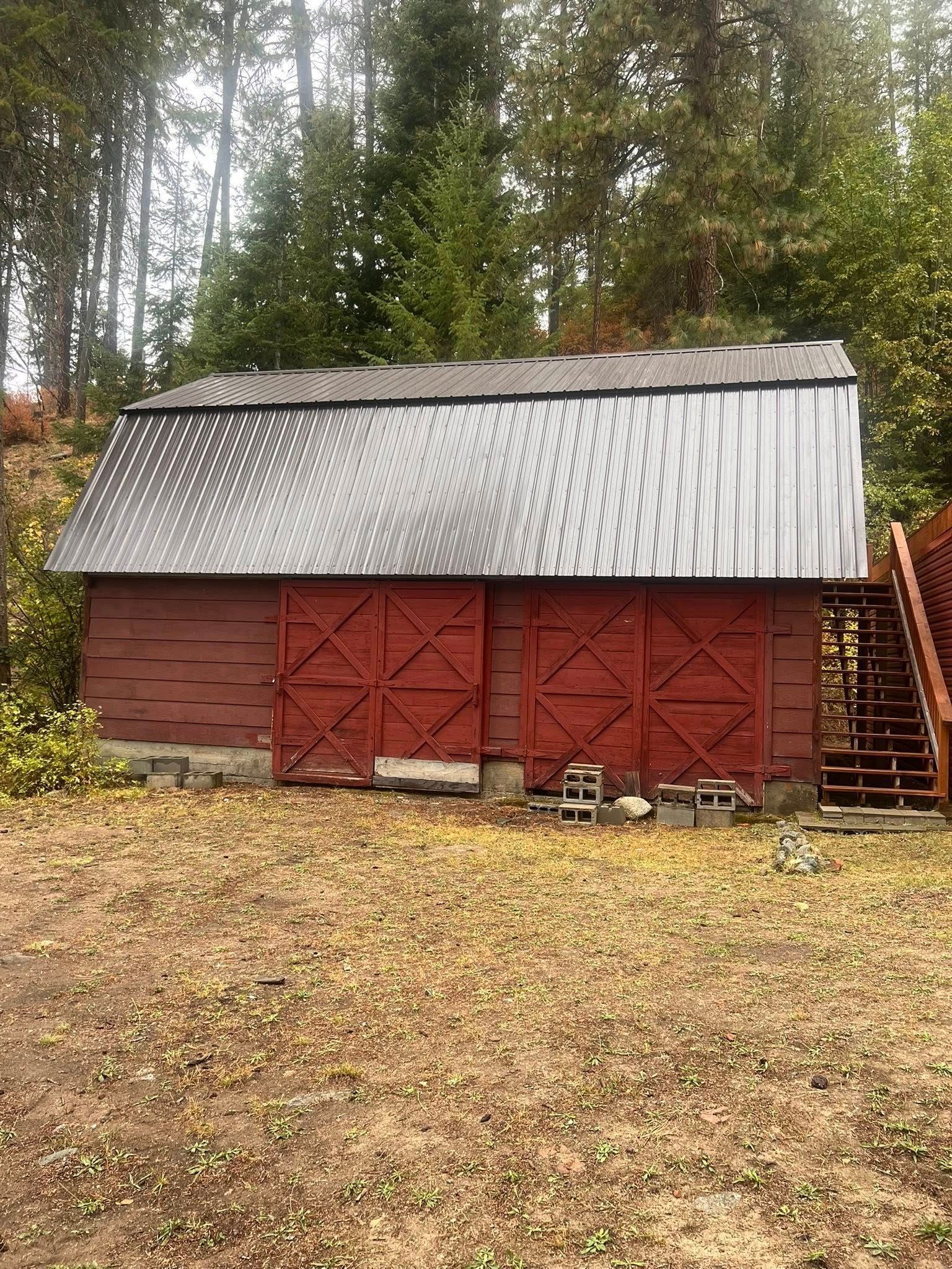 Red barn with sliding doors and corrugated metal roof, in a yard with scattered leaves, surrounded by trees.