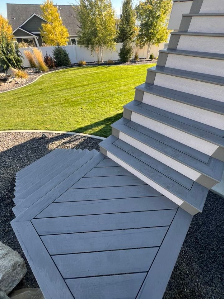 Gray deck and stairs lead to a grassy yard with a house.