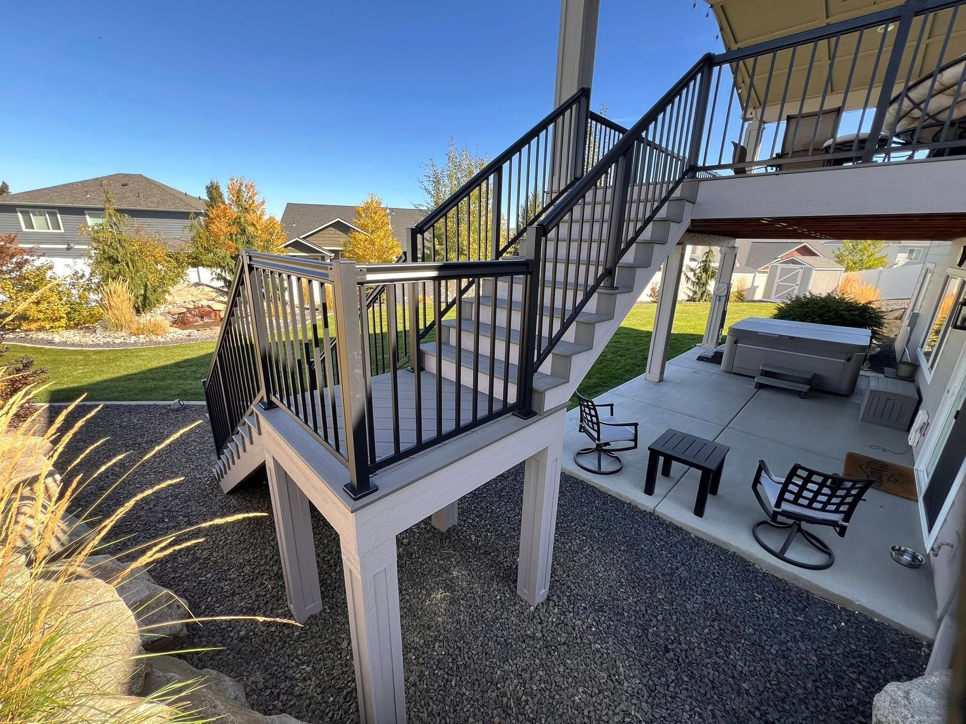 Outdoor deck with stairs, black railing, light gray supports, and backyard.