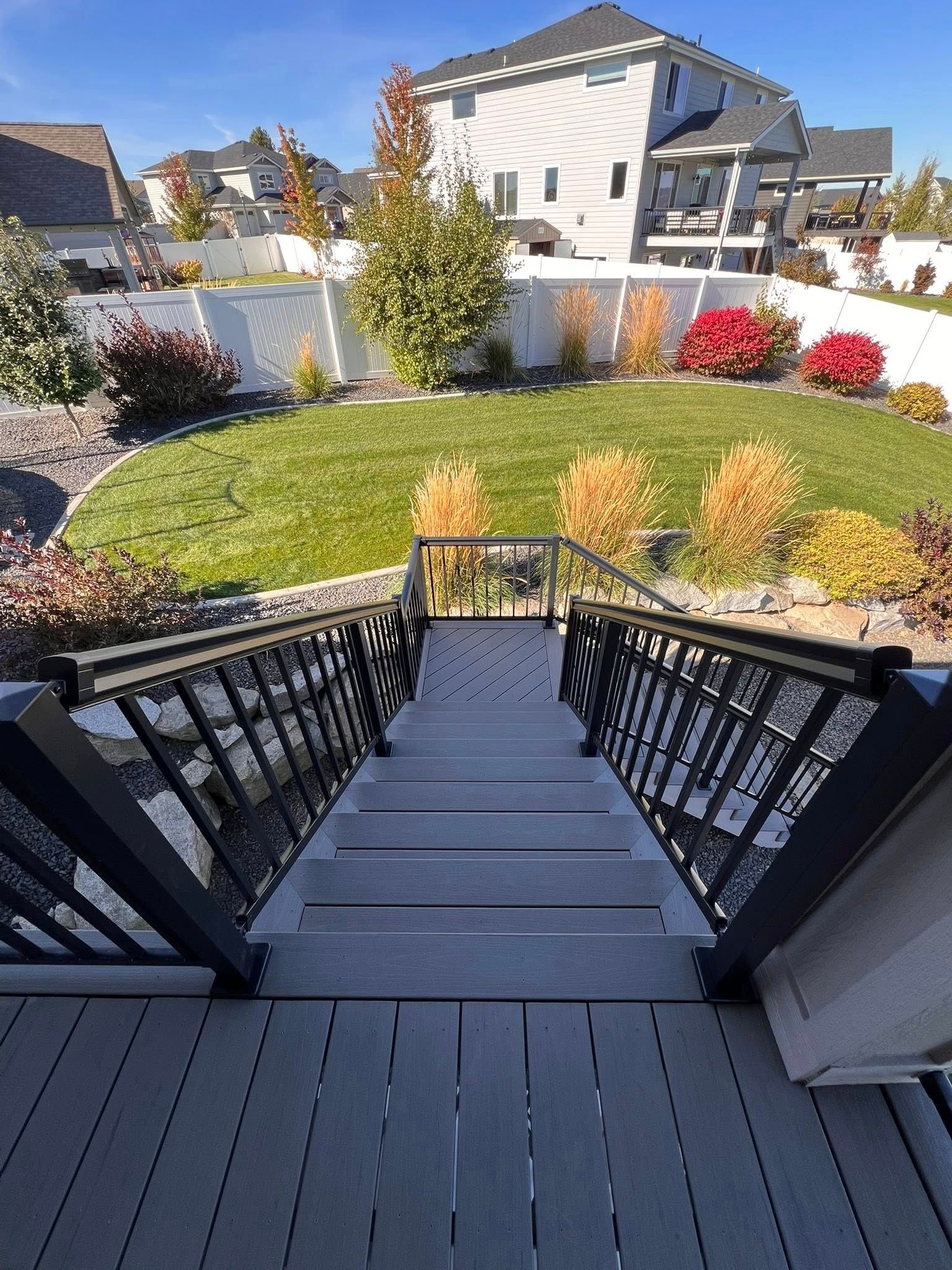 Wooden deck stairs leading to a backyard with grass, colorful bushes, and houses in the distance.