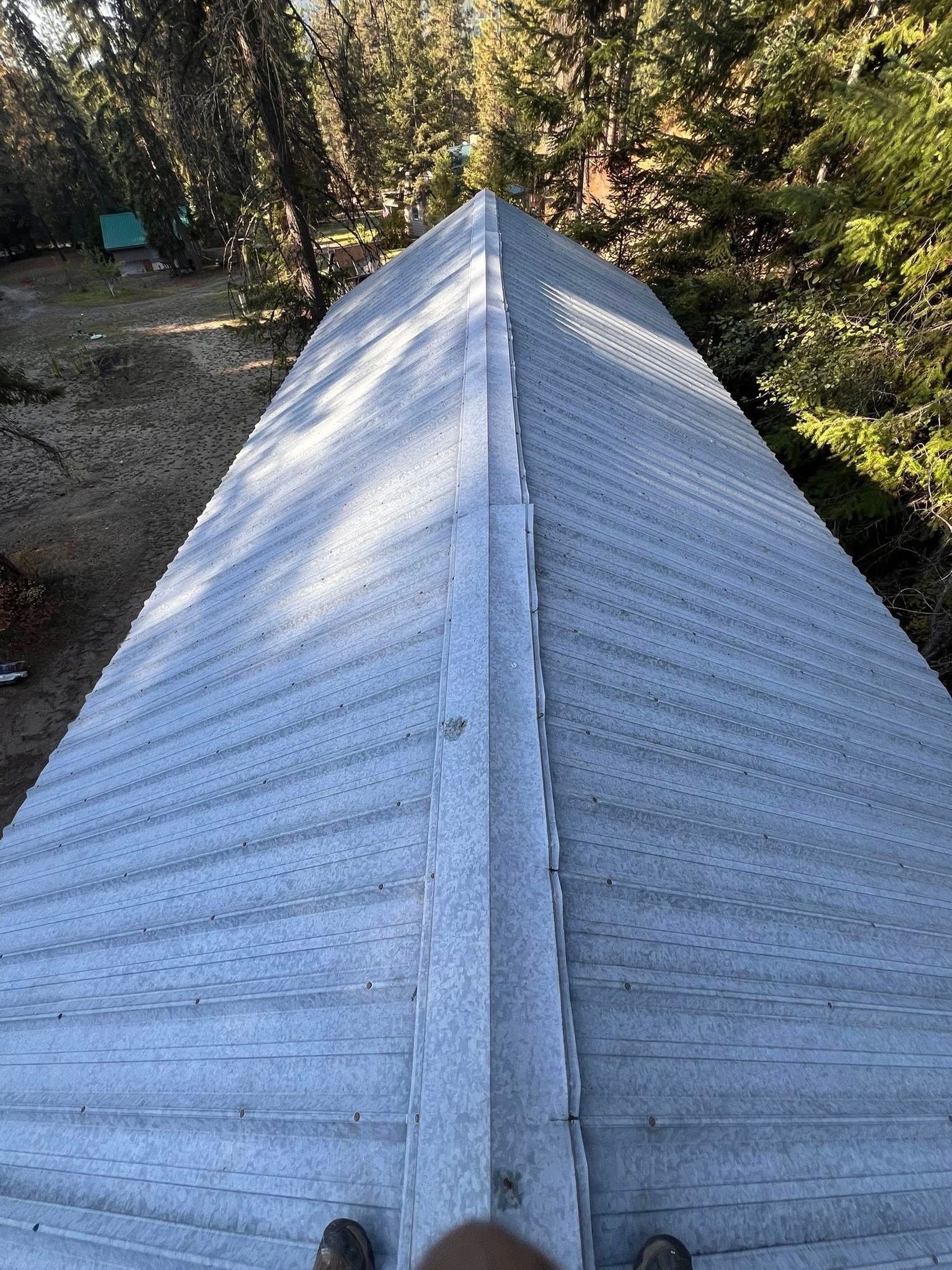 View from above of a metal roof with a peak. Trees in the background.