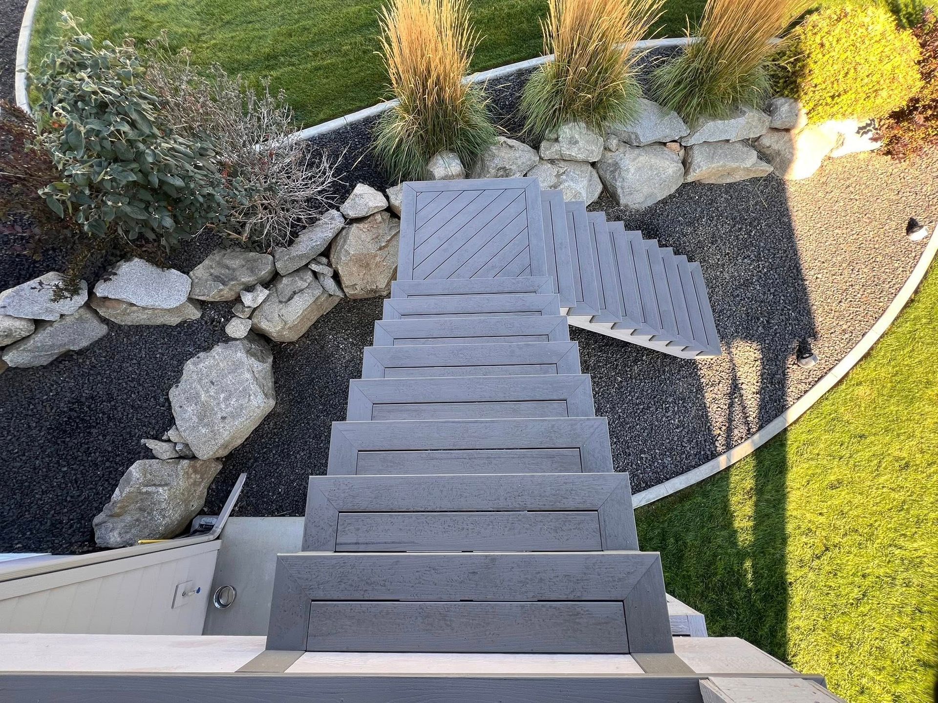 Gray outdoor staircase descending into a landscaped yard with rocks, plants, and grass.