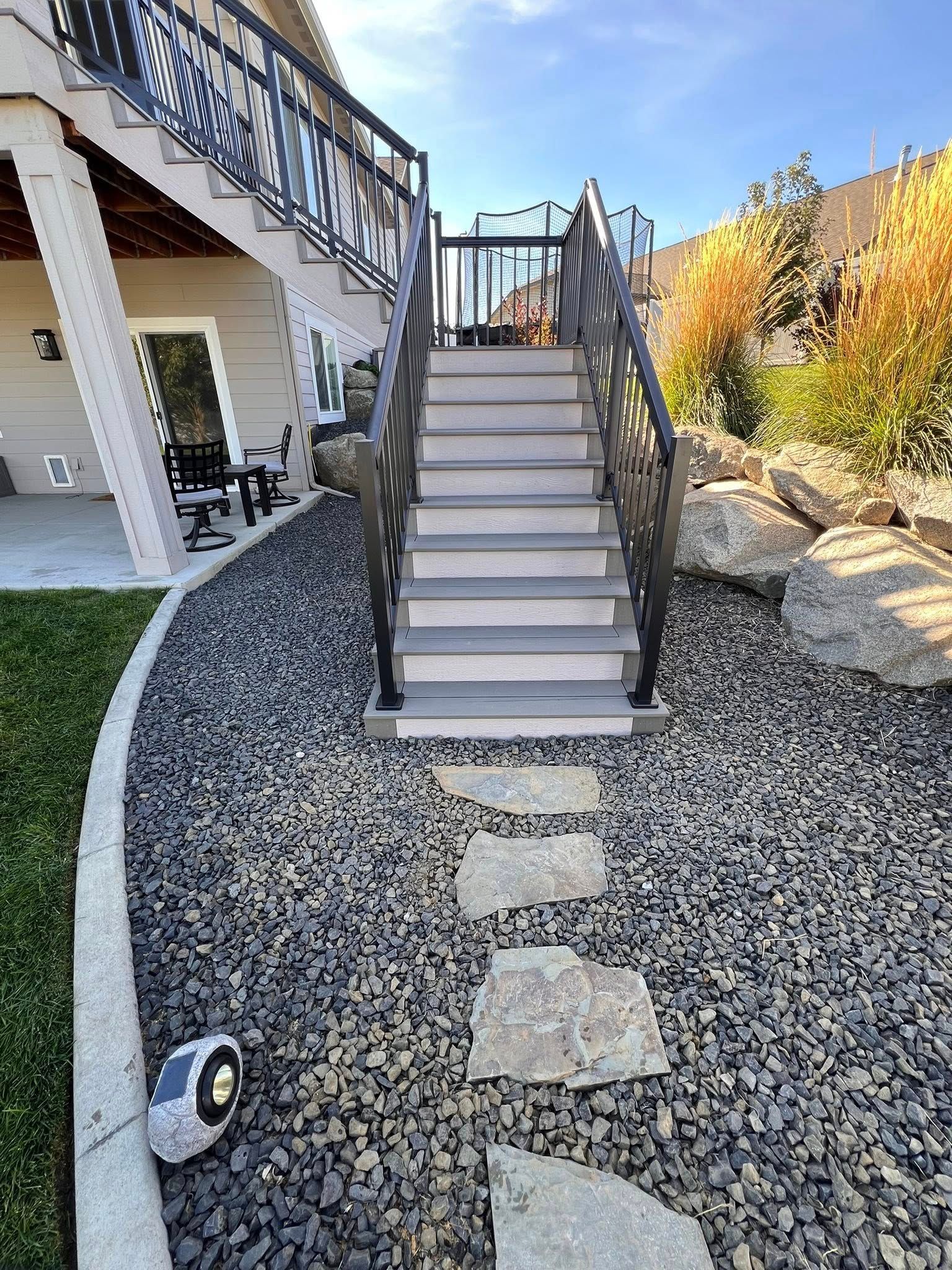 Staircase leading up to a deck with decorative black railings. Pathway of rocks and stepping stones on a sunny day.