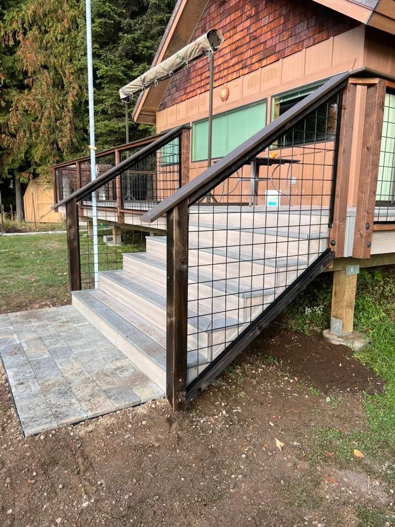 Wooden steps with dark metal railing leading up to a cabin with a brown shingled facade.