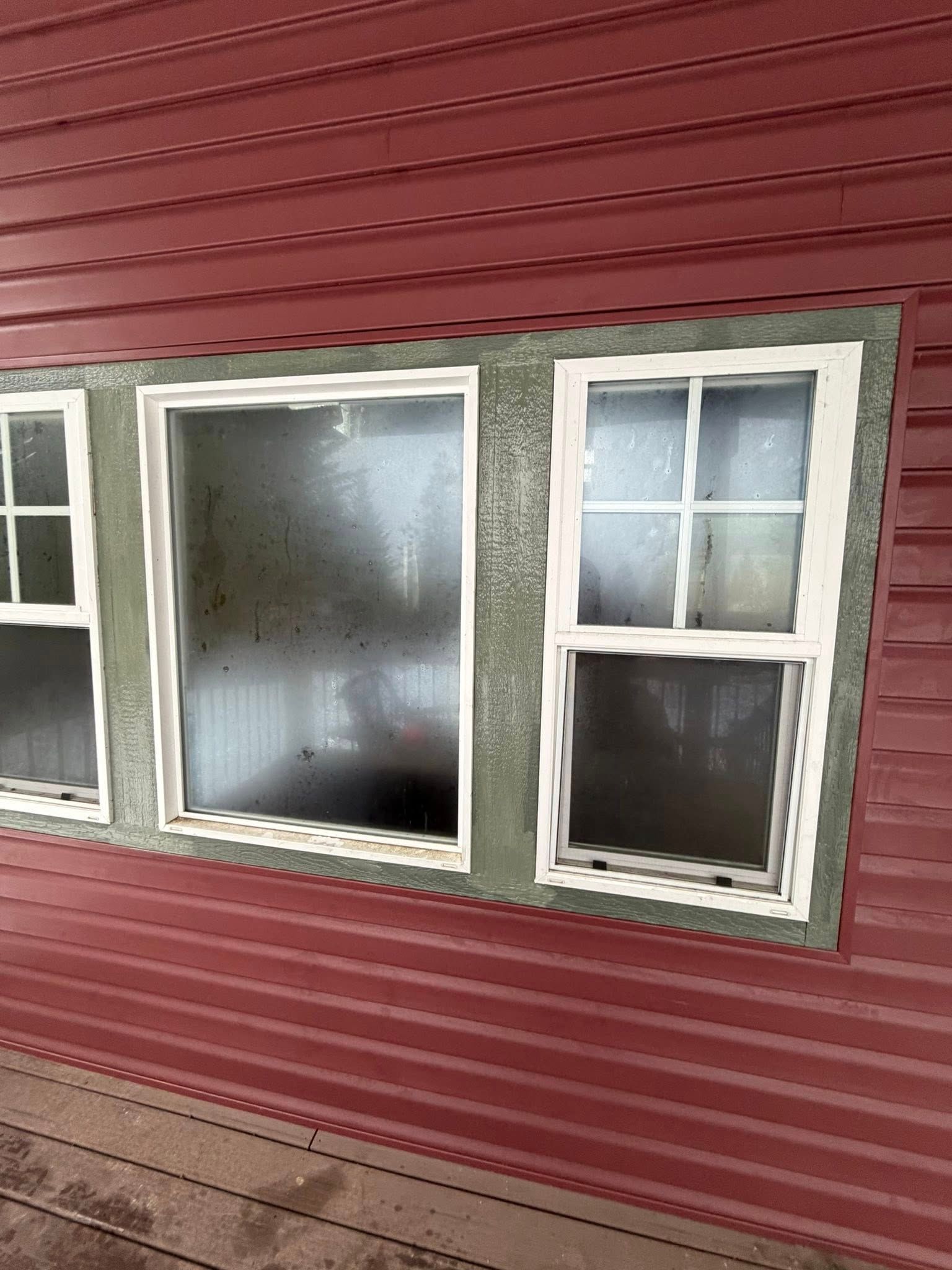 Three windows with white frames on a red paneled wall. Green painted trim surrounds the windows.