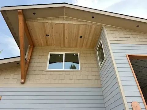 Exterior of a house with light blue, beige, and tan siding.  A wooden beam supports the overhang.