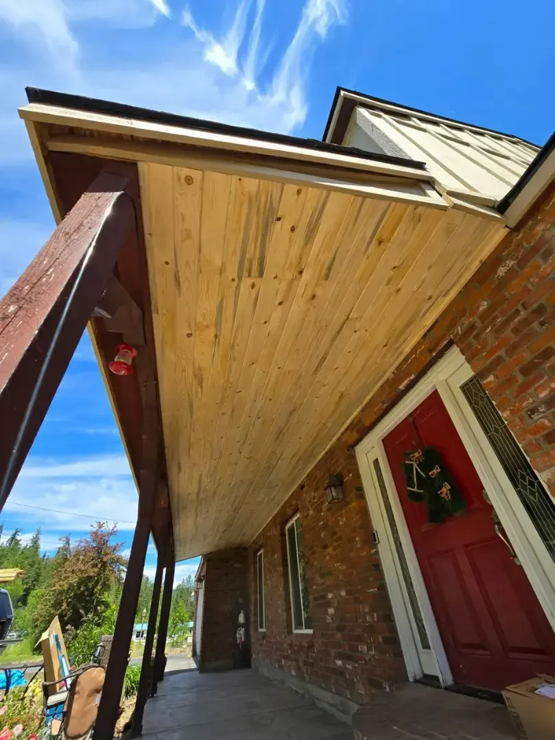 A porch with a wooden ceiling and red door on a brick building, under a blue sky with streaky clouds.