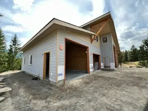 A two-story house under construction with a garage. Gray siding, tan trim, and a cloudy sky.